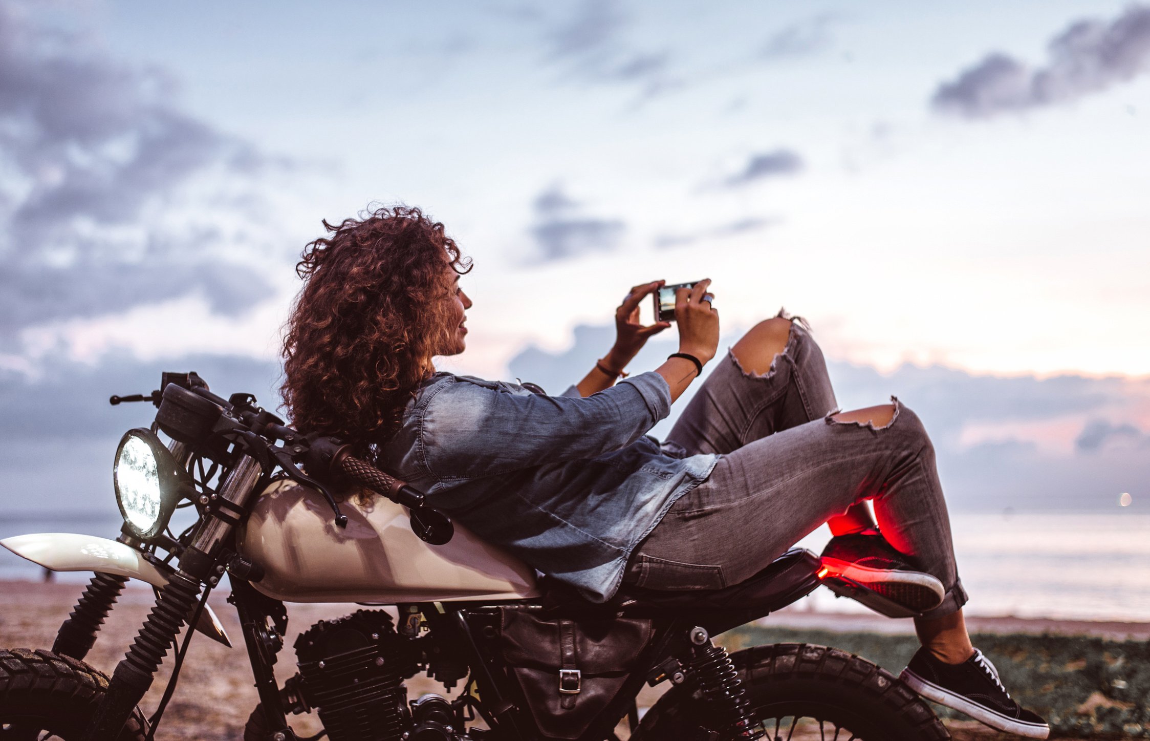 Girl on a Motorcycle Taking a Picture of the Sunset